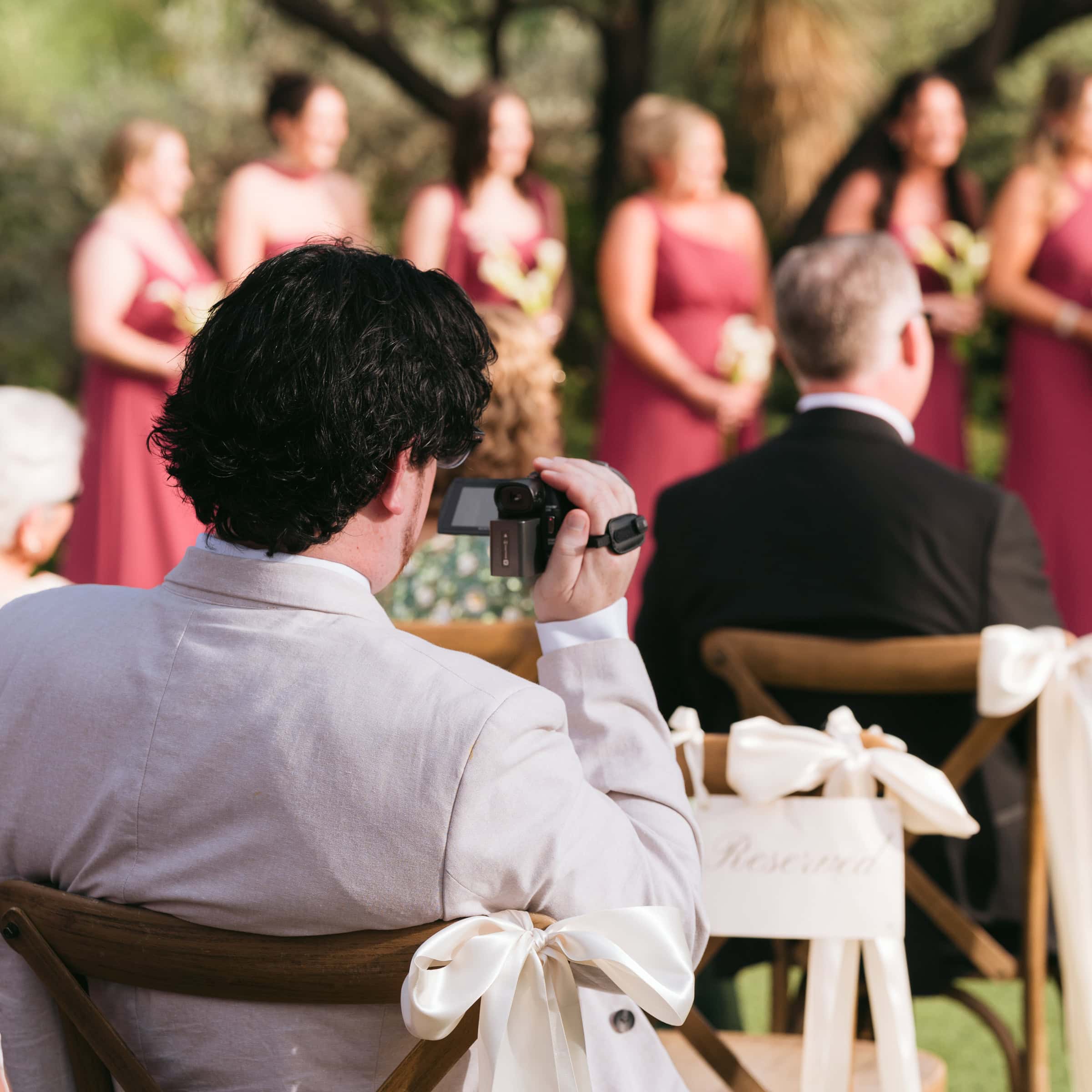 Wedding guest filming an outdoor ceremony with a handheld camcorder